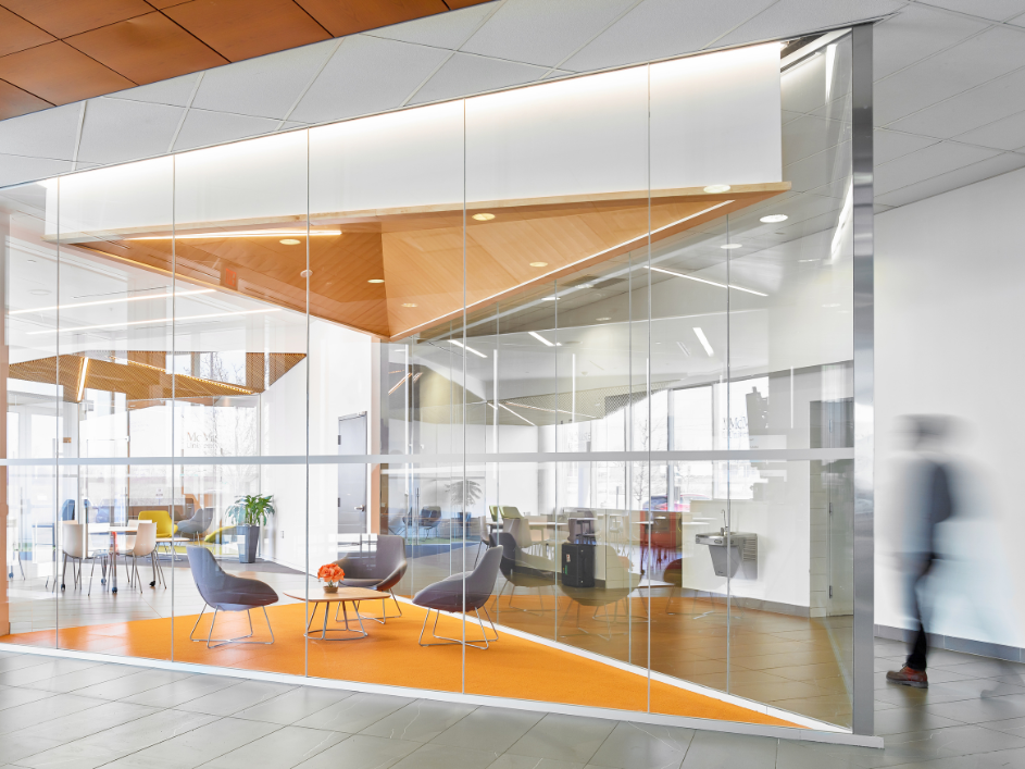 An modern common space with chairs and a table, enclosed by glass walls.